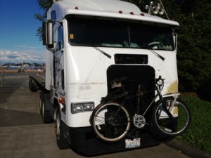 Semi-truck tractor with a bike in a rack on the front of the truck.
