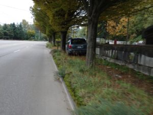 Photo of car parked on dirt path on west side of West Marginal Way Southwest where there is no street parking and no paved sidewalk.